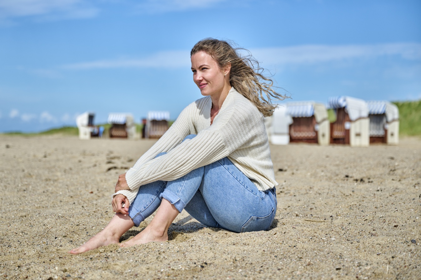 Frau sitzt im Sand am Strand von Cuxhaven