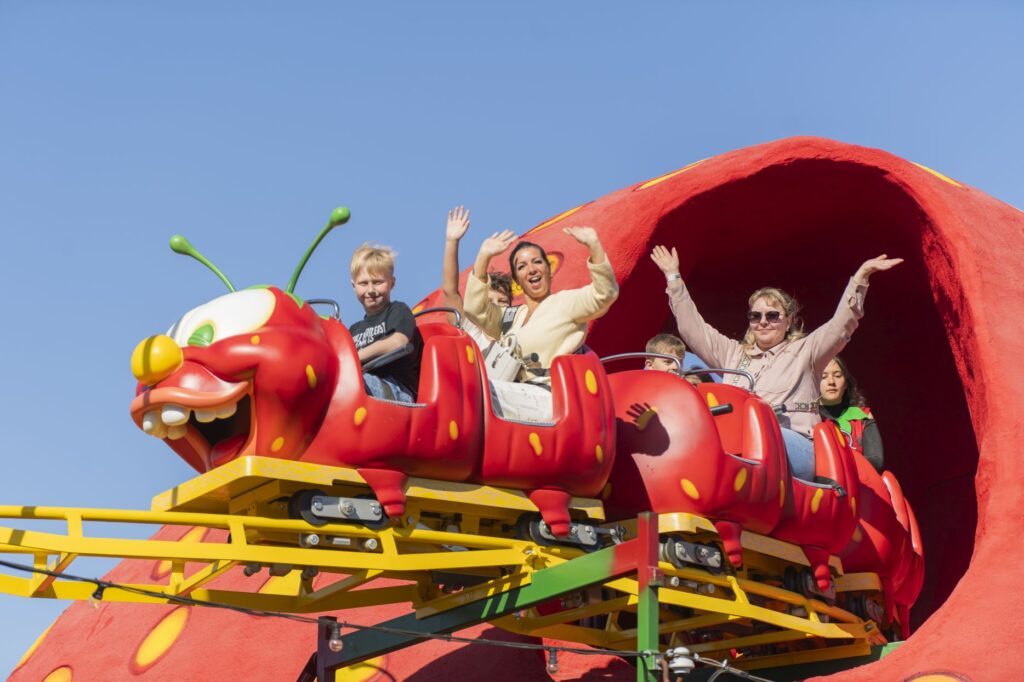 Mehrere Personen sitzen in einer Achterbahn und winken in Richtung Kamera.