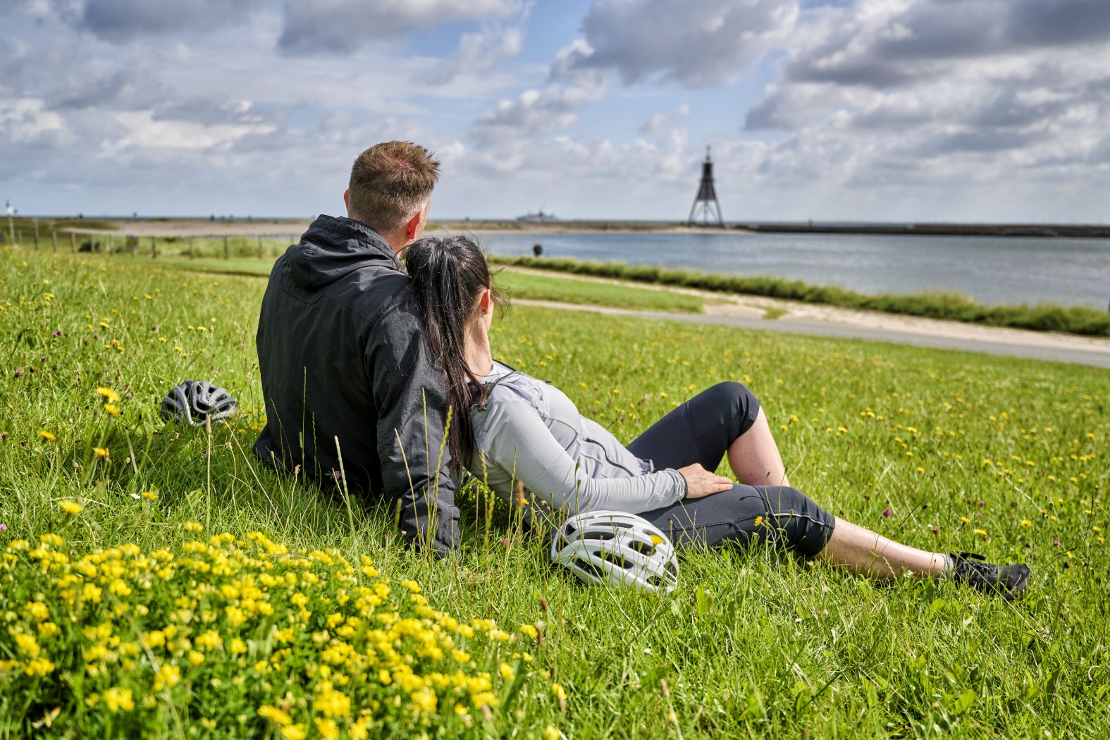 Zwei Radfahrer machen eine Pause auf einer Wiese am Wasser.