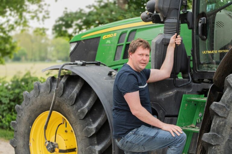 Landwirt steht vor einem Traktor und schaut in die Kamera.