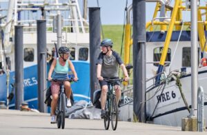 Zwei Radfahrer mit Booten im Hintergrund.