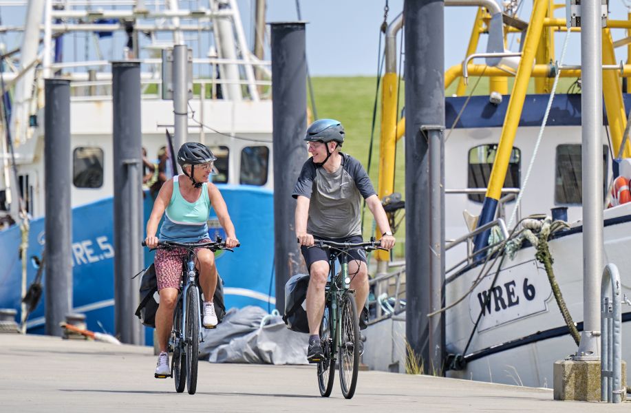 Zwei Radfahrer mit Booten im Hintergrund.