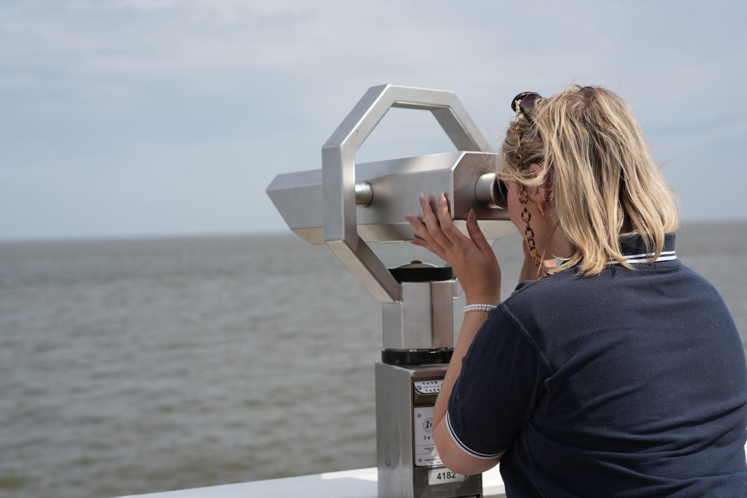 Frau steht an einem Fernglas und schaut auf das Wasser.