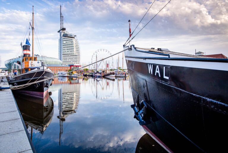 Mehrere Schiffe liegen im neuen Hafen in Bremerhaven. Im Hintergrund sind markante Gebäude und Sehenswürdigkeiten zu erkennen: das Klimahaus, ein Hotel sowie ein großes Riesenrad.
