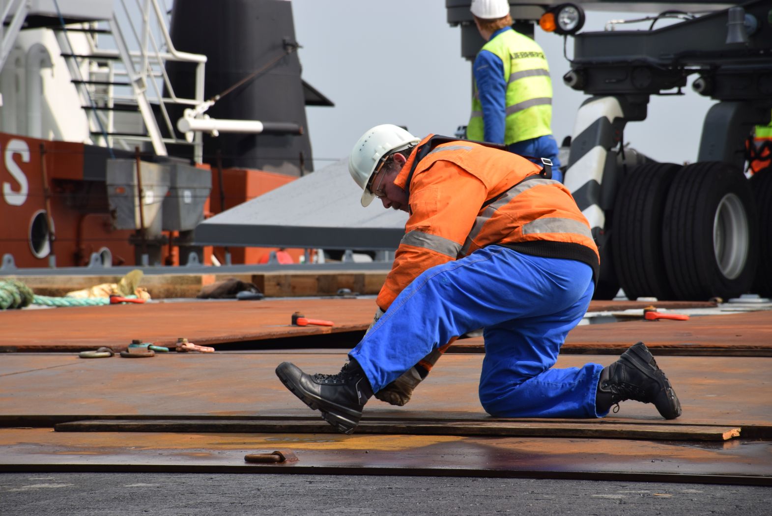Person mit Schutzhelm kniet auf dem Boden und arbeitet.