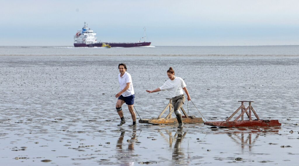 Tim Seebach (links, Oliver Mommsen) und Hannah Lübker (rechts, Ulrike C. Tscharre) beim traditionellen Schlickschlittenrennen im Watt.